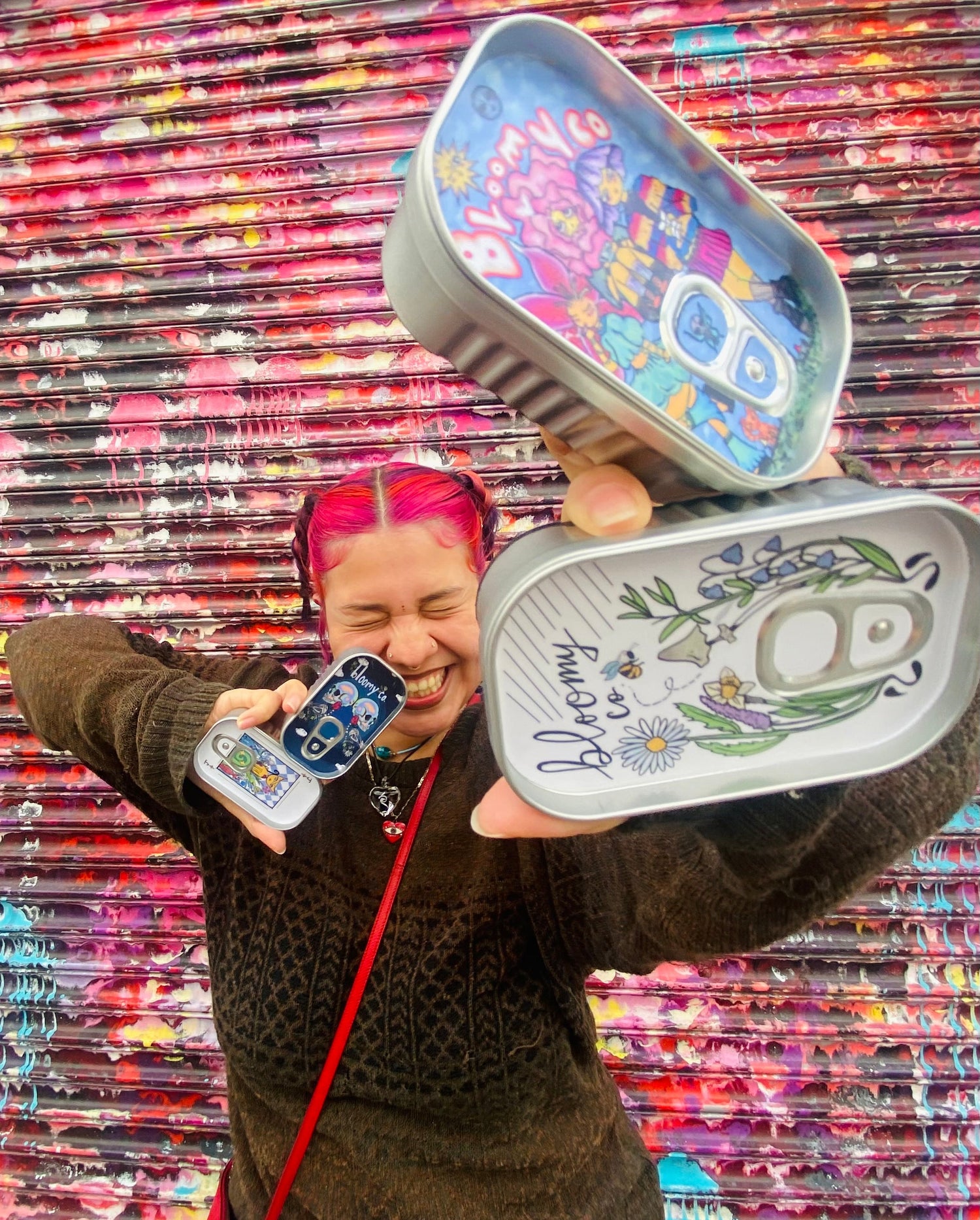 Person holding four decorative stash kit tins with a colorful, textured wall in the background